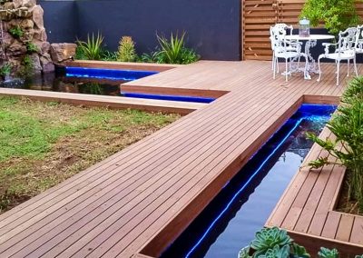 Lush backyard oasis with large water feature and shaded seating in Durban by Creative Landscapes