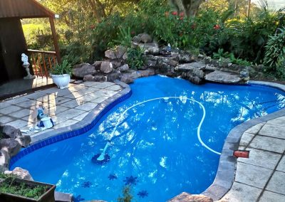Swimming pool with built-in rock water feature and tropical landscaping in Durban, installed by Creative Landscapes